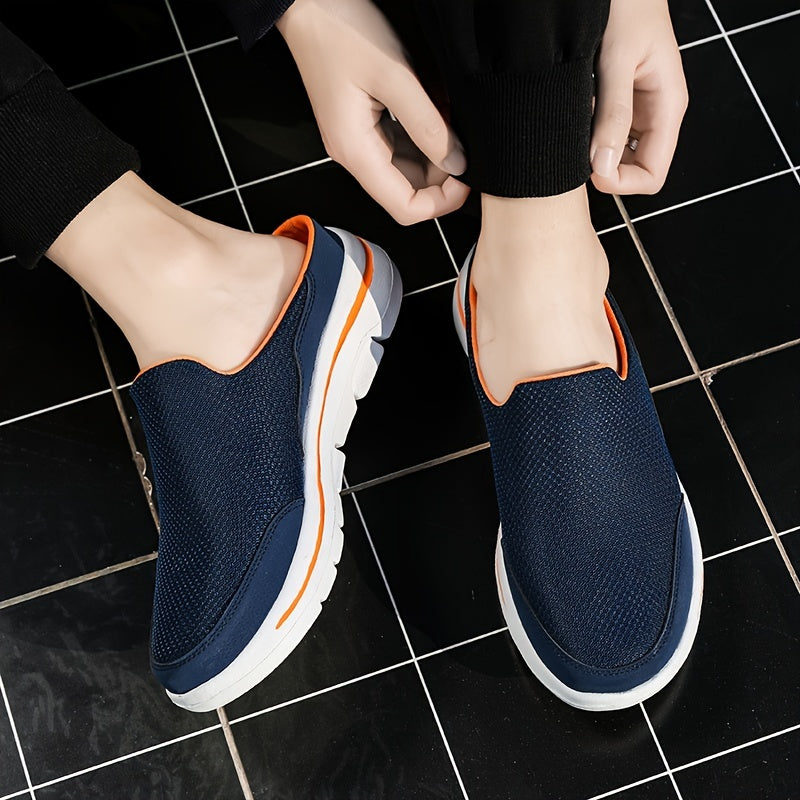 Person trägt blaue Slip-On-Sneaker mit weißer Sohle und orangefarbenen Akzenten auf schwarzem Fliesenboden. Bequeme Freizeitschuhe für Herren.