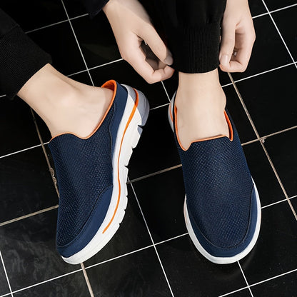Person trägt blaue Slip-On-Sneaker mit weißer Sohle und orangefarbenen Akzenten auf schwarzem Fliesenboden. Bequeme Freizeitschuhe für Herren.