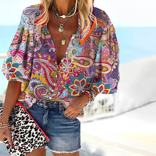 Frau in bunter Paisley-Bluse und Jeansshorts am Strand, hält eine Leoparden-Clutch. Sommermode, Boho-Stil, Strandoutfit, modische Accessoires.
