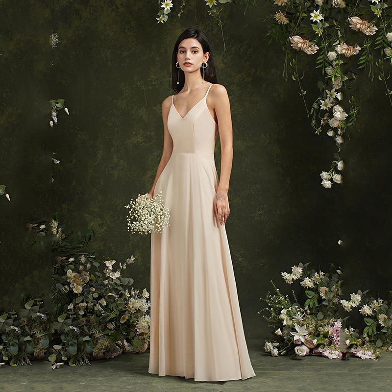 Frau in elegantem, cremefarbenem Abendkleid mit Blumenstrauß, umgeben von grüner, blumiger Kulisse. Perfekt für Hochzeits- oder Abendmode.