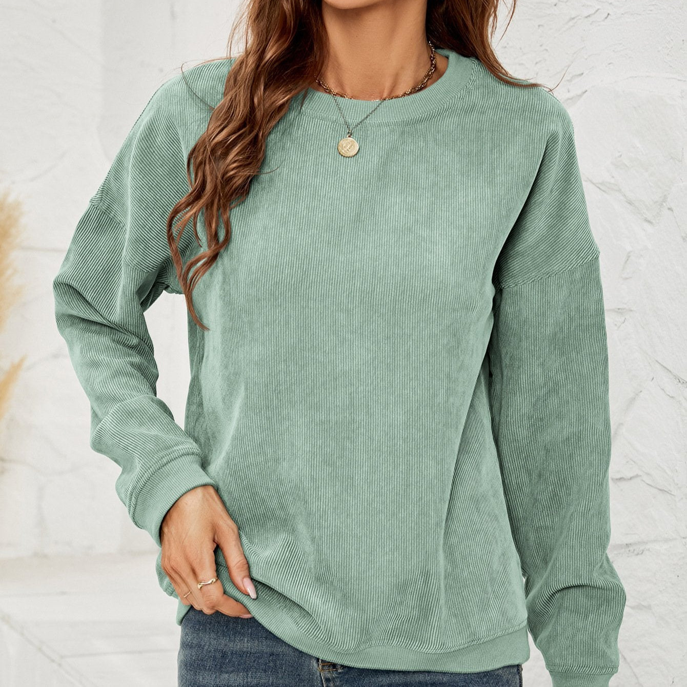 Frau in grünem Cordpullover, lässiger Stil, modisches Outfit, Herbstmode, langärmlig, entspannter Look, weiße Wand im Hintergrund.