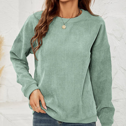 Frau in grünem Cordpullover, lässiger Stil, modisches Outfit, Herbstmode, langärmlig, entspannter Look, weiße Wand im Hintergrund.