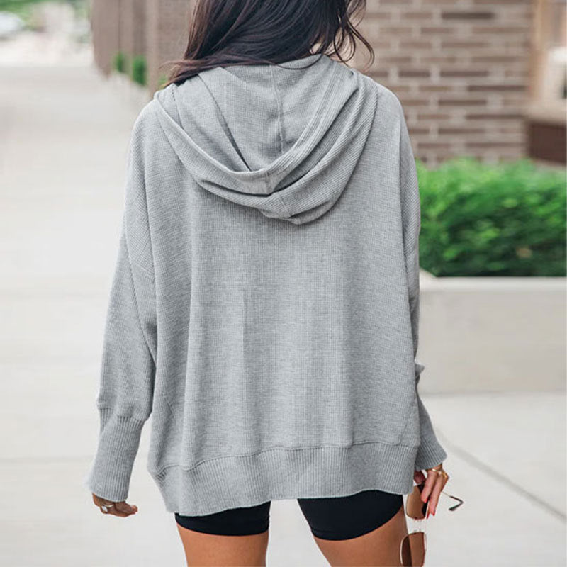 Frau in grauem Hoodie und schwarzen Shorts von hinten, lässiger Streetstyle, urbaner Hintergrund, modische Freizeitkleidung.