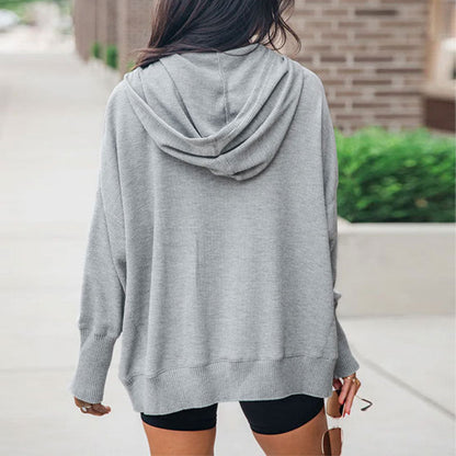 Frau in grauem Hoodie und schwarzen Shorts von hinten, lässiger Streetstyle, urbaner Hintergrund, modische Freizeitkleidung.