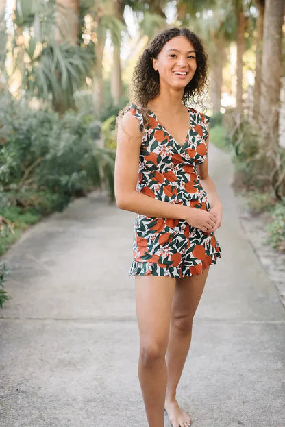 Junge Frau in geblümtem Sommerkleid steht barfuß auf einem Weg, umgeben von tropischen Pflanzen. Lächelnd, Freizeitmode, Naturkulisse.