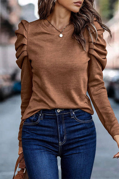 Frau in braunem Pullover mit Rüschenärmeln und blauer Jeans auf Straße. Modetrend, Herbstmode, stilvolle Damenbekleidung.