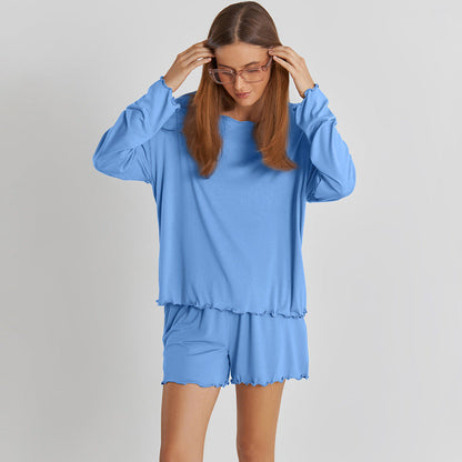 Frau in blauer Loungewear, bestehend aus langärmligem Oberteil und Shorts, mit Brille. Bequeme Damenmode, Freizeitkleidung, entspannter Stil.