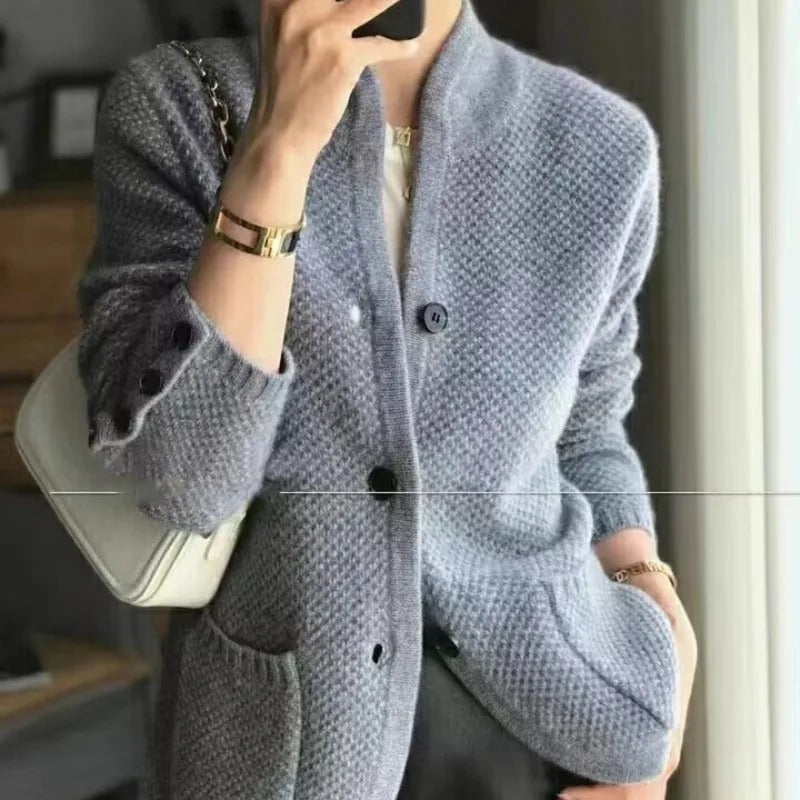 Grauer Strick-Cardigan mit Knöpfen, getragen von einer Person, kombiniert mit weißer Handtasche und goldenen Accessoires. Elegante Herbstmode.
