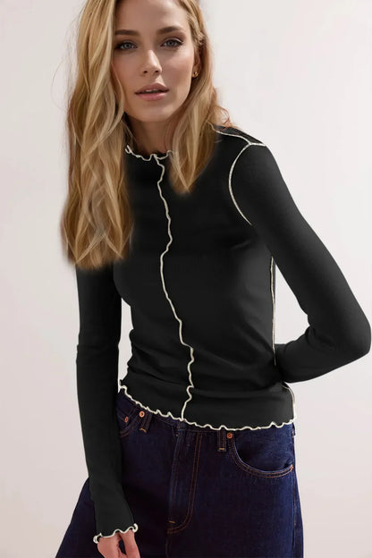 Blonde Frau in schwarzem Langarmshirt mit weißen Rüschen, kombiniert mit blauen Jeans. Modetrend, stilvolle Damenbekleidung, Freizeitlook.