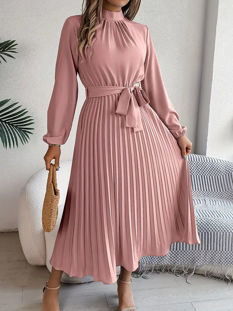 Elegantes rosa Plisseekleid mit langen Ärmeln und Taillengürtel, getragen von einer Frau, die eine Strohtasche hält. Perfekt für Frühling und Sommermode.