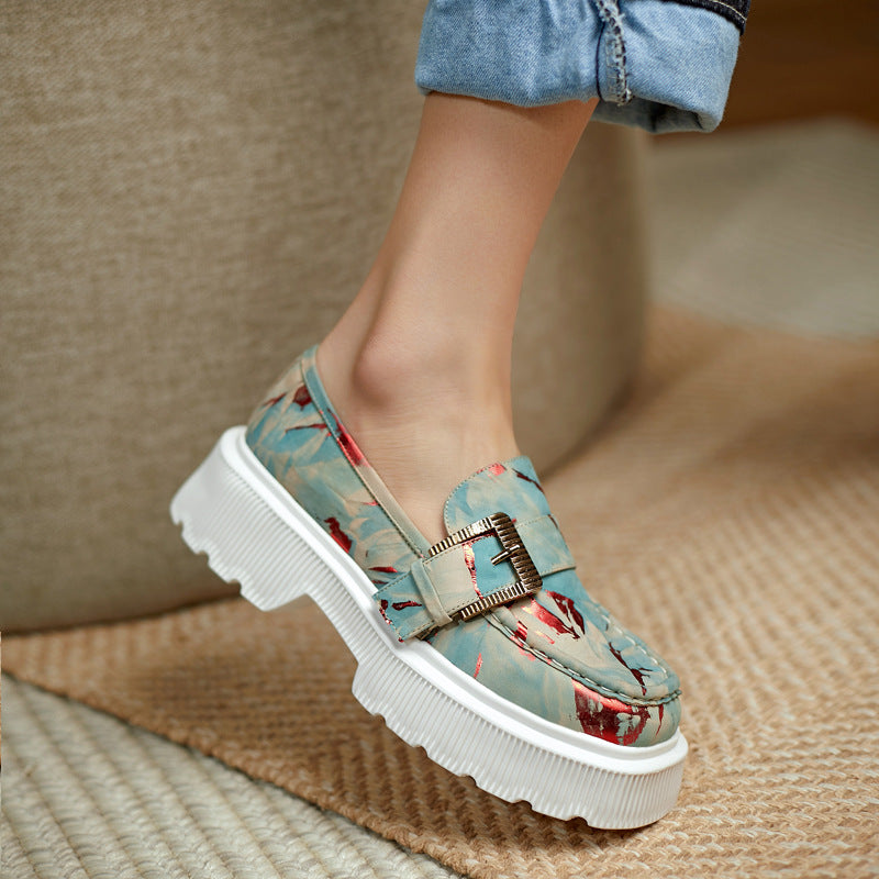 Damen-Loafer mit floralem Muster, goldener Schnalle und dicker weißer Sohle, getragen mit hochgekrempelter Jeans auf beigem Teppich.