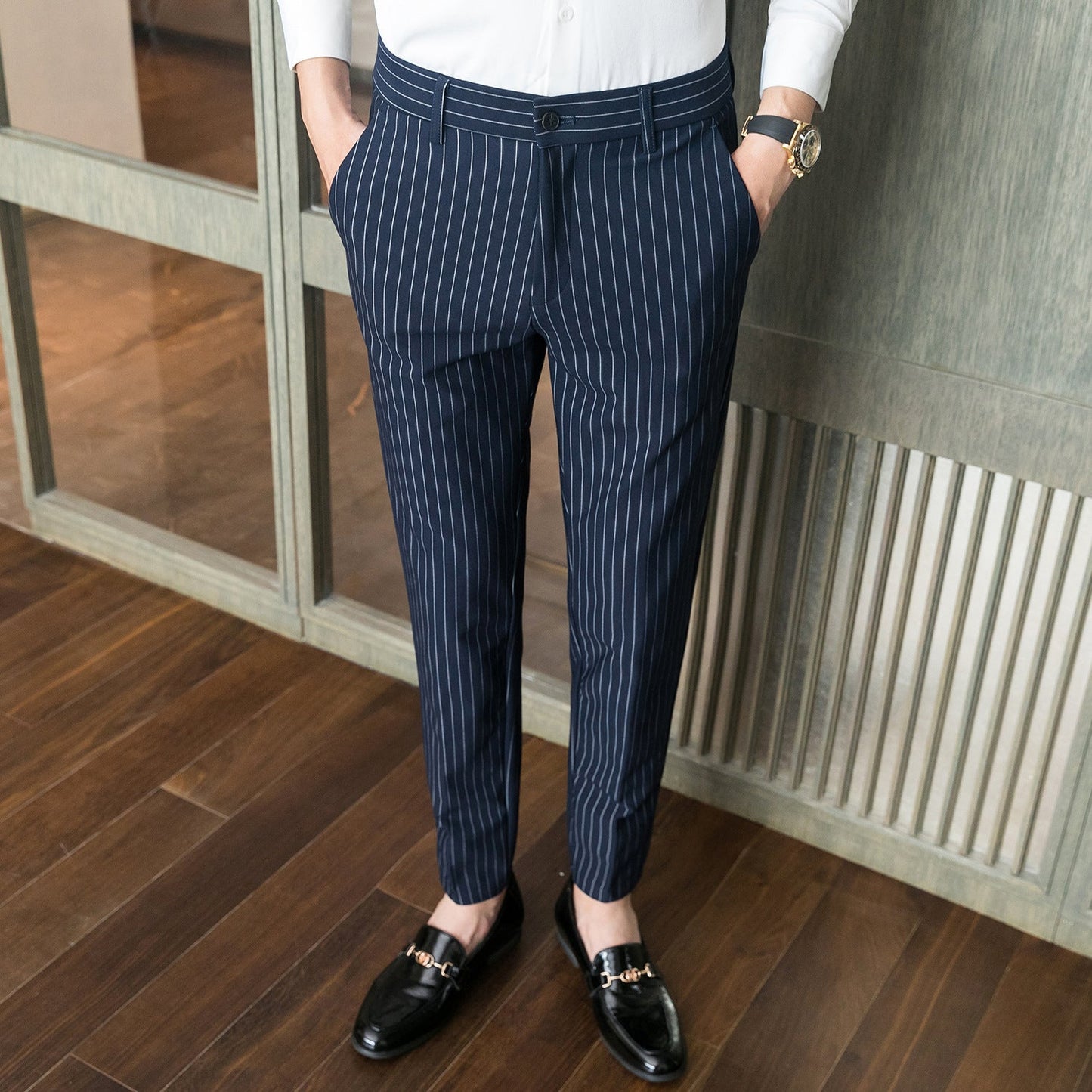 Mann in eleganter, gestreifter Anzughose, weißem Hemd und schwarzen Loafern auf Holzboden. Businessmode, Herrenbekleidung, stilvoller Look.