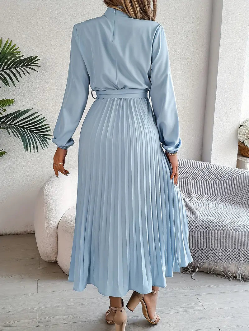 Frau in hellblauem, langem, plissiertem Kleid, steht in modernem Wohnzimmer. Elegantes Modeoutfit, Rückansicht, stilvolle Inneneinrichtung.