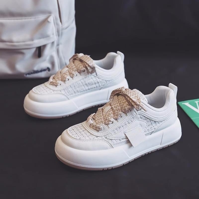 Weiße Sneaker mit dicker Sohle und beige gemusterten Schnürsenkeln auf schwarzem Hintergrund, neben einem weißen Rucksack.