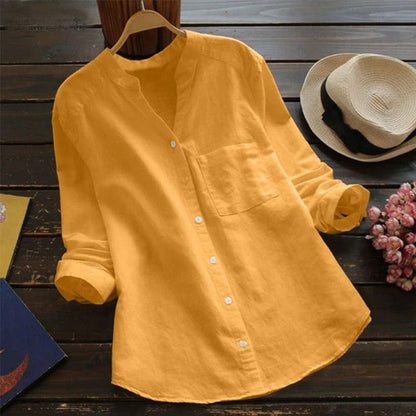 Gelbes Leinenhemd mit Stehkragen und Brusttasche auf Holztisch, neben Strohhut und Blumen. Perfekt für lässige Sommermode.