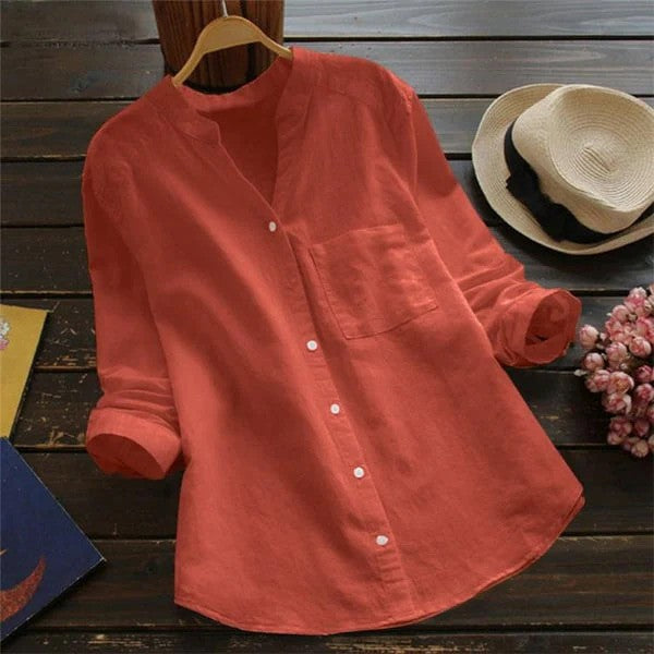 Rote Damenbluse aus Leinen mit Stehkragen und Knopfleiste, auf Holztisch mit Strohhut und Blumen. Elegante Freizeitmode, Frühling/Sommer.