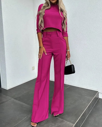 Frau in pinkem Hosenanzug mit weitem Bein und bauchfreiem Oberteil, hält schwarze Handtasche. Modetrend, elegante Damenmode, stilvolles Outfit.