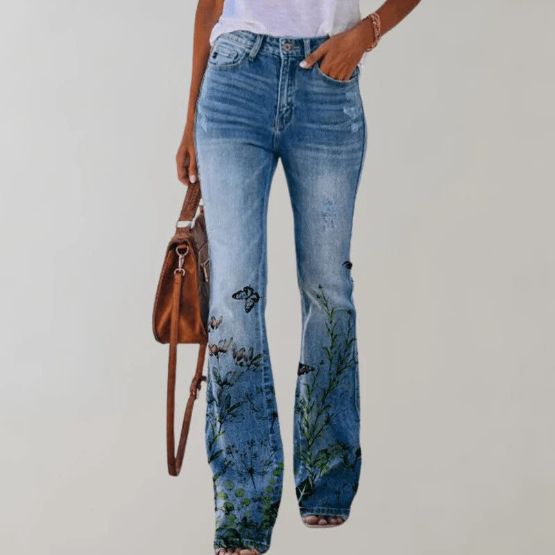 Damenjeans mit Blumenstickerei, Schmetterlingsmotiv und ausgestelltem Bein, kombiniert mit weißem T-Shirt und brauner Ledertasche.