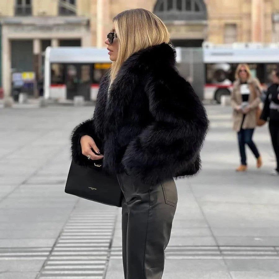 Frau in schwarzer Pelzjacke und Lederhose, hält eine schwarze Handtasche, steht auf städtischem Platz. Elegante Wintermode, stilvolle Accessoires.