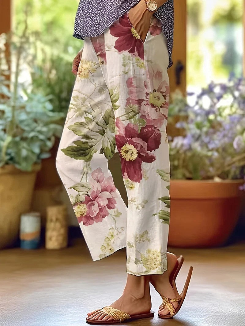 Frau trägt weiße, geblümte Sommerhose mit großen roten und grünen Blumen, kombiniert mit geflochtenen Sandalen. Perfekt für lässige Sommermode.