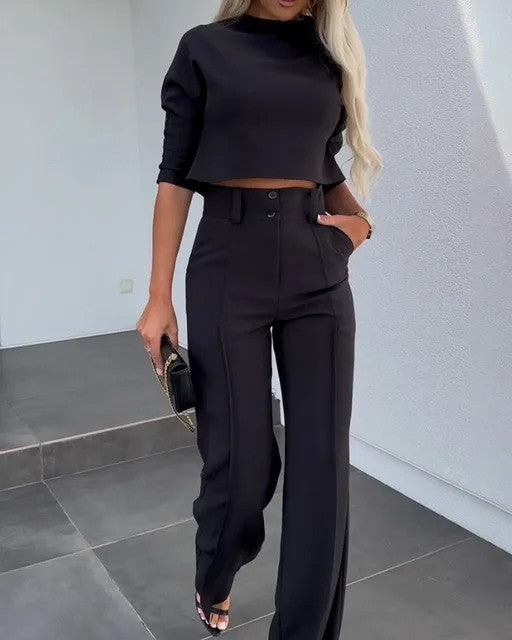 Elegante Frau in schwarzem Crop-Top und Hose, steht auf grauen Fliesen. Modetrend, Damenmode, stilvolles Outfit, moderne Kleidung.
