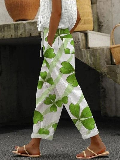 Frau trägt weiße Hose mit grünem Kleeblattmuster, kombiniert mit weißem Oberteil und Sandalen. Modetrend, lässiger Sommerlook, Streetstyle.