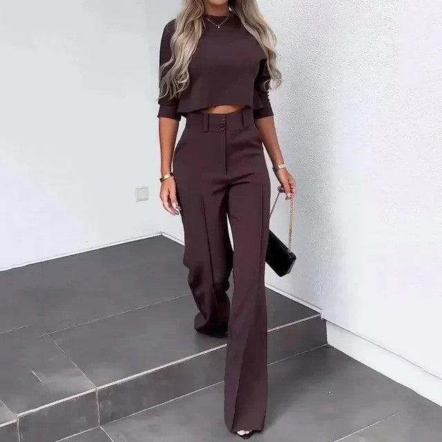 Frau in eleganter, dunkelbrauner Hose und passendem Crop-Top, trägt schwarze Handtasche. Modetrend, stilvolle Damenbekleidung, Herbstmode.
