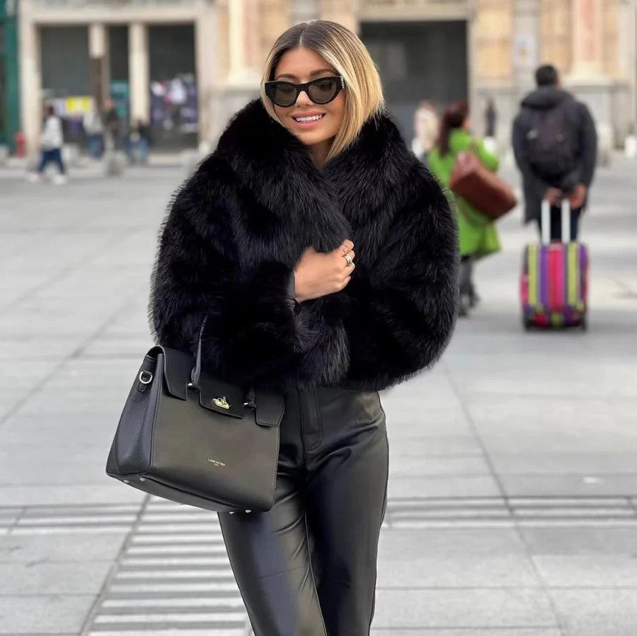 Frau in schwarzem Pelzmantel und Sonnenbrille, trägt schwarze Lederhose und Handtasche, steht auf belebtem Platz. Mode, Winteroutfit, Stadtleben.