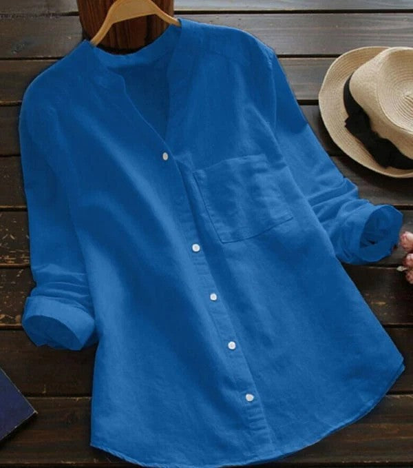 Blaue Leinenbluse auf Holztisch, neben Strohhut. Modische Damenbekleidung, lässiger Stil, ideal für Sommer. Elegante, knitterfreie Bluse.