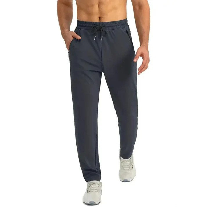 Mann in dunkelgrauer Jogginghose, sportlich, mit Kordelzug und Taschen, trägt weiße Turnschuhe. Ideal für Fitness und Freizeit.
