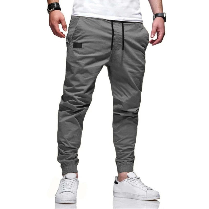 Graue Jogginghose für Herren, modern geschnitten, mit elastischem Bund und Bündchen, kombiniert mit weißen Sneakers. Ideal für Freizeitmode.