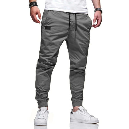 Graue Jogginghose für Herren, modern geschnitten, mit elastischem Bund und Bündchen, kombiniert mit weißen Sneakers. Ideal für Freizeitmode.