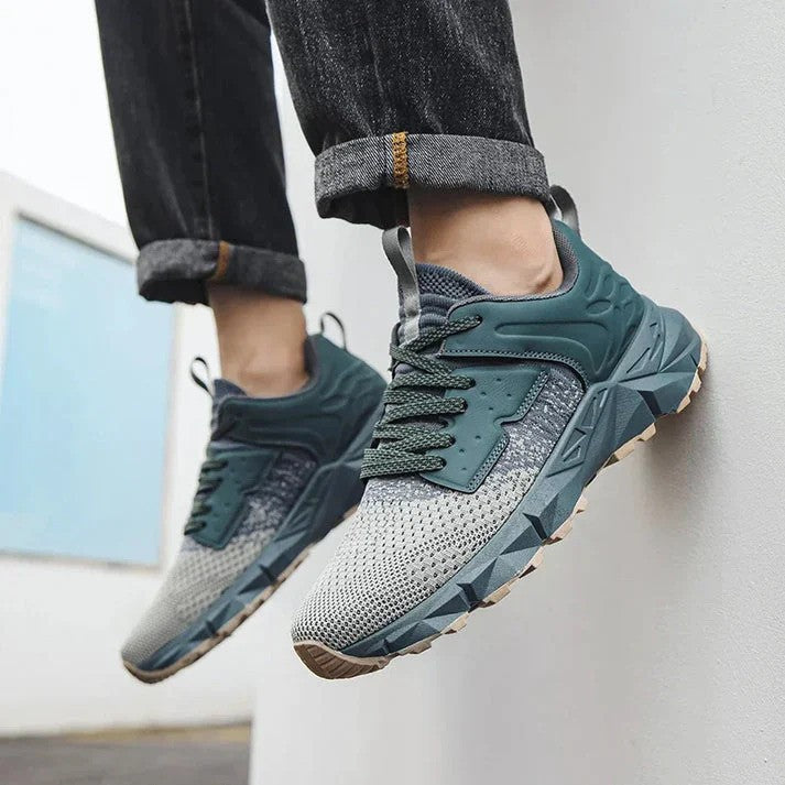 Graue und grüne Sneaker an den Füßen einer Person in Jeans, moderne Sportschuhe, Outdoor-Design, bequeme Passform, ideal für Freizeit und Sport.