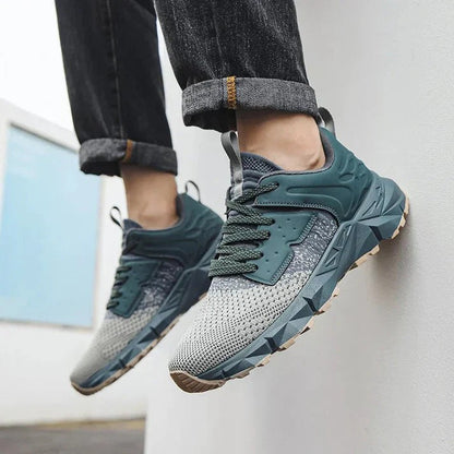 Graue und grüne Sneaker an den Füßen einer Person in Jeans, moderne Sportschuhe, Outdoor-Design, bequeme Passform, ideal für Freizeit und Sport.