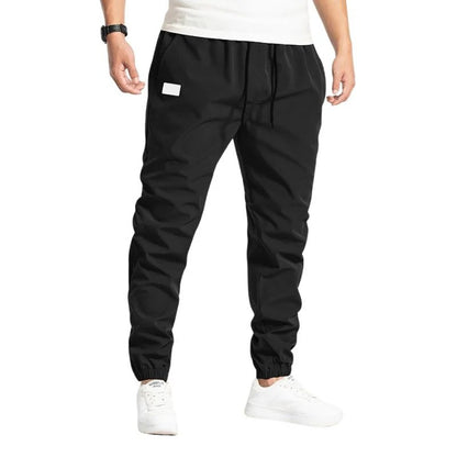 Schwarze Jogginghose für Herren, elastischer Bund, weiße Sneakers, sportlich, bequem, ideal für Fitness und Freizeit.