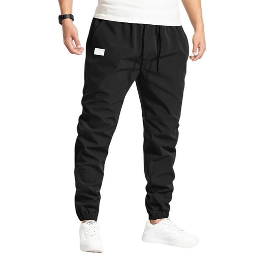 Schwarze Jogginghose für Herren, elastischer Bund, weiße Sneakers, sportlich, bequem, ideal für Fitness und Freizeit.