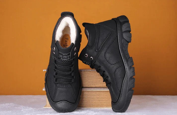 Schwarze Wanderschuhe mit robustem Profil auf Holzkiste vor orangefarbenem Hintergrund. Outdoor-Schuhe, rutschfest, bequem, langlebig.
