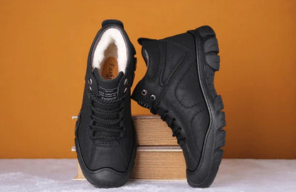 Schwarze Wanderschuhe mit robustem Profil auf Holzkiste vor orangefarbenem Hintergrund. Outdoor-Schuhe, rutschfest, bequem, langlebig.