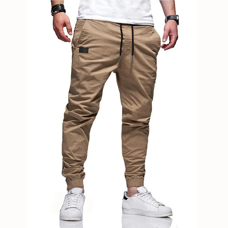 Beige Jogginghose für Herren, lässig geschnitten, mit elastischem Bund und Kordelzug, kombiniert mit weißen Sneakers. Ideal für Freizeitmode.