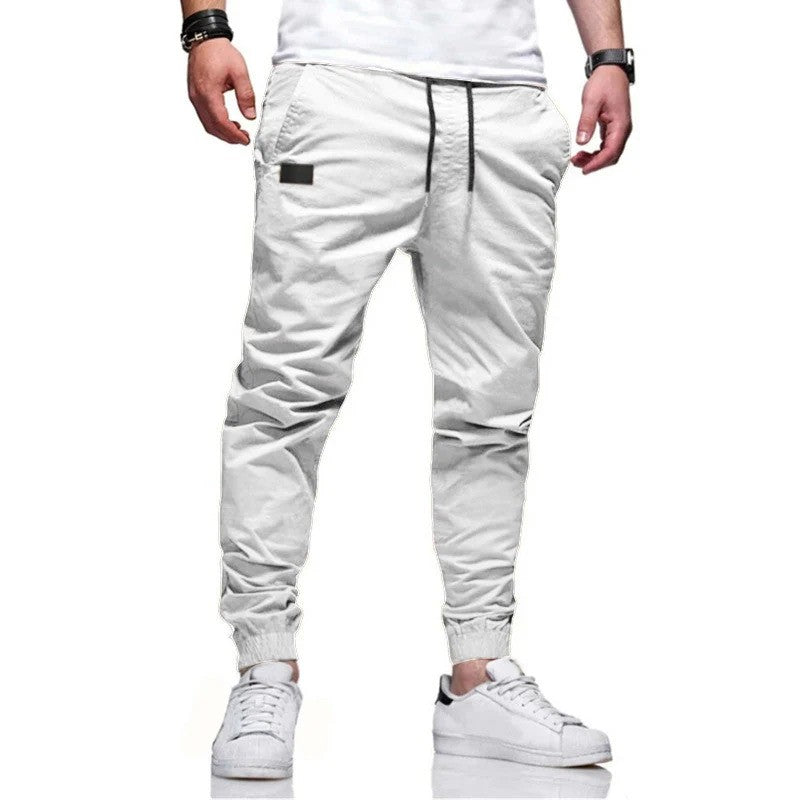Weiße Jogginghose für Herren, modern geschnitten, mit Kordelzug und elastischen Bündchen, kombiniert mit weißen Sneakers. Ideal für Freizeitmode.