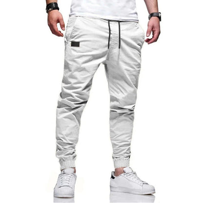 Weiße Jogginghose für Herren, modern geschnitten, mit Kordelzug und elastischen Bündchen, kombiniert mit weißen Sneakers. Ideal für Freizeitmode.