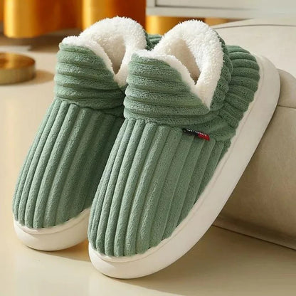 Grüne, plüschige Hausschuhe mit weißem Futter auf beigem Hintergrund. Bequeme, warme Pantoffeln für den Winter. Ideal für gemütliche Abende.