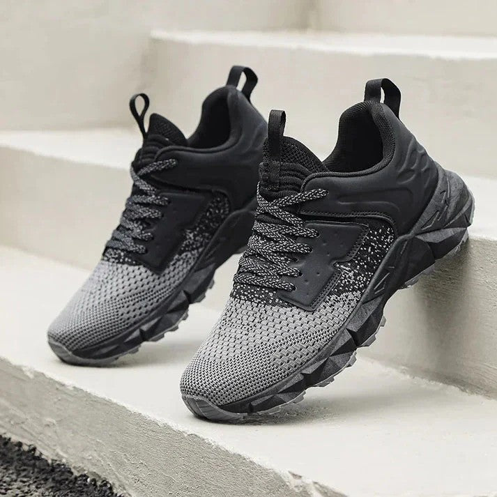 Graue und schwarze Sportschuhe auf Treppe, atmungsaktives Mesh-Obermaterial, rutschfeste Sohle, ideal für Laufen und Fitness.