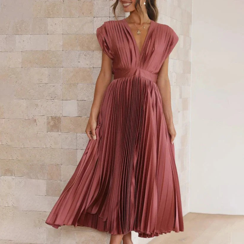 Frau in elegantem, plissiertem, rosafarbenem Kleid mit tiefem V-Ausschnitt vor beiger Steinwand. Modetrend, Abendmode, Damenkleidung.