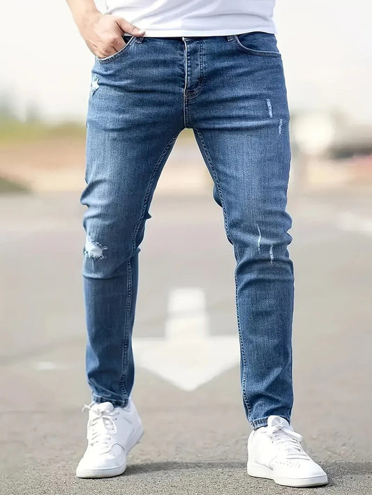 Mann in blauer, zerrissener Jeans und weißen Sneakers auf Straße. Modetrend, Herrenjeans, Freizeitlook, urbaner Stil.
