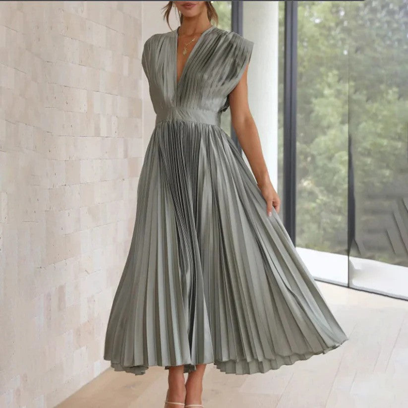 Elegantes, graues, plissiertes Kleid mit V-Ausschnitt, ärmellos, knielang, getragen von einer Frau in modernem, minimalistischem Innenraum.