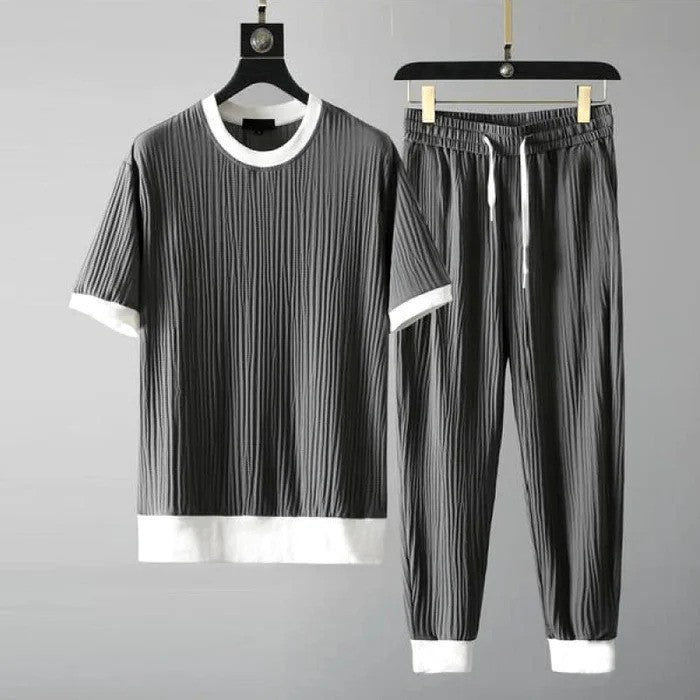 Graues Herren-Set aus T-Shirt und Jogginghose mit weißen Bündchen, geripptes Design, lässige Mode, bequemes Freizeitoutfit, auf Kleiderbügeln.