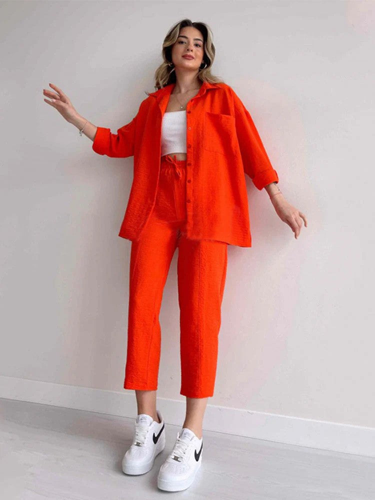 Frau in leuchtend rotem Outfit mit weißem Top und weißen Nike-Sneakers, posiert vor weißer Wand. Modetrend, Streetstyle, Damenmode.