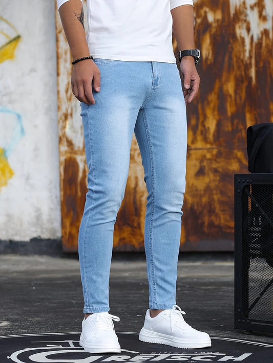 Mann in hellblauer Jeans und weißen Sneakers vor rostiger Wand. Modische Herrenbekleidung, lässiger Stil, urbane Mode.