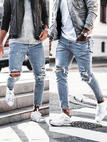 Zwei Männer in zerrissenen Jeans und weißen Sneakers, einer trägt eine schwarze Lederjacke, der andere eine graue Bomberjacke, gehen auf der Straße.